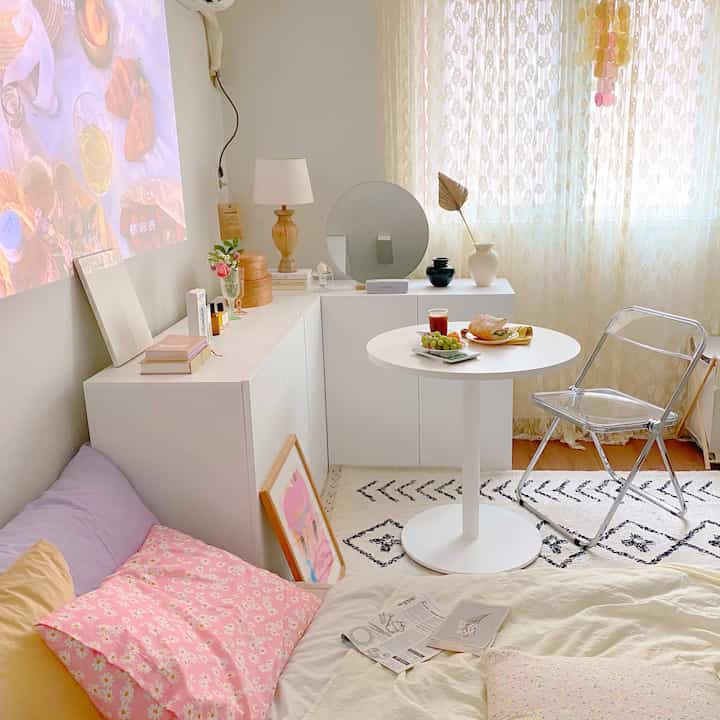White-toned studio apartment featuring a round dining table and transparent chair with a cozy, bright atmosphere