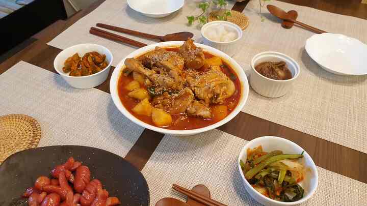 Wood tone dining table in kitchen featuring Korean spicy braised chicken and various side dishes arranged neatly