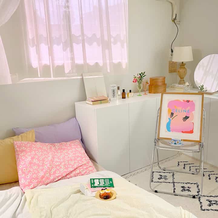 A bright white and pink toned studio bedroom featuring a clean storage cabinet and art frame, creating a natural atmosphere