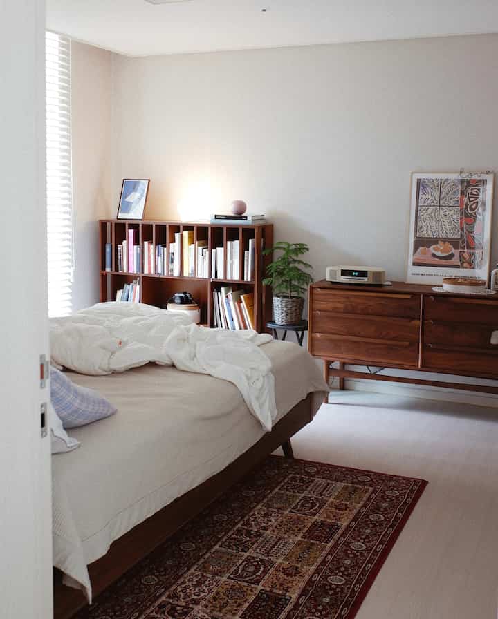 White-walled bedroom with wood tone furniture, tidy dresser and bookshelf, cozy rug in a natural modern setting