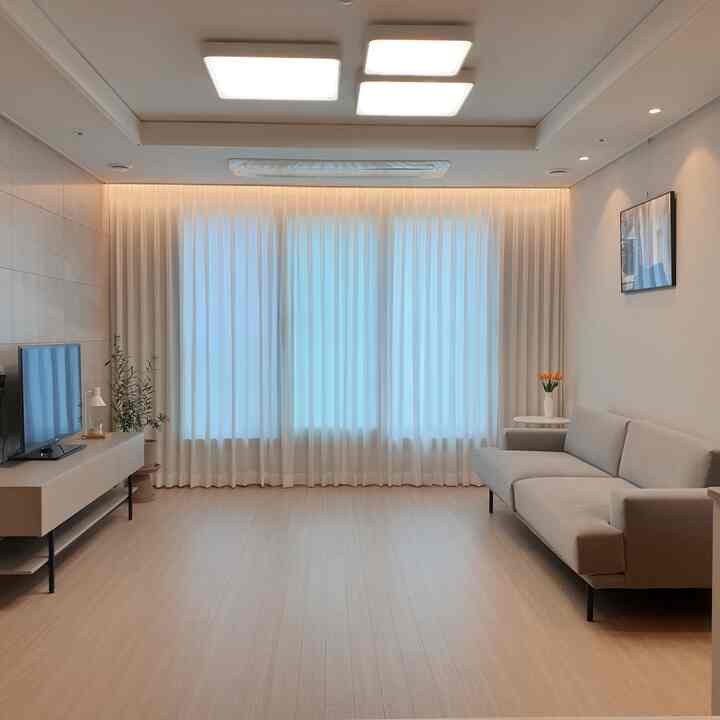 A simple living room with beige flooring and sofa, accented by black metal legs and picture frames