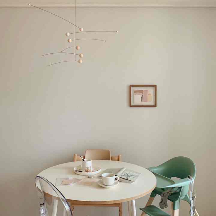 ベージュとホワイトの色調のダイニングスペース、モビールとベビー用ハイチェアが配置された自然でモダンなインテリア