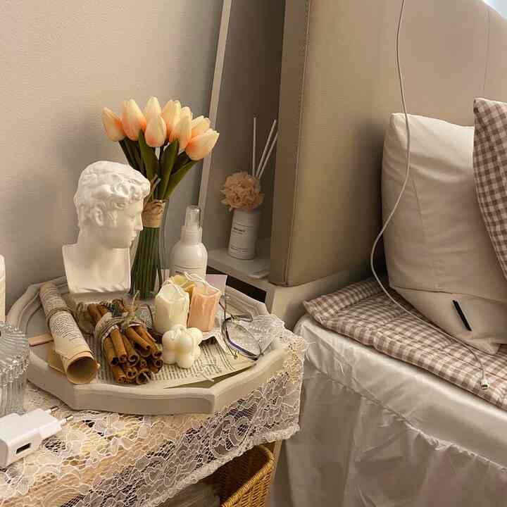 Beige-toned bedroom featuring a nightstand with a plaster bust, candles, cinnamon sticks, and a vase, creating a warm and natural decor atmosphere