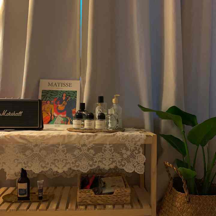 Soft natural-toned bedroom featuring ivory blackout curtains, a wooden shelf with fragrance products, and a rattan basket for a cozy atmosphere