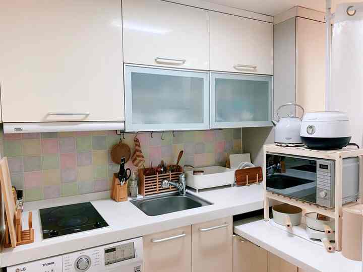 Compact 10-pyeong kitchen in white and natural wood tones, featuring organized storage items and an eyelet curtain for space division