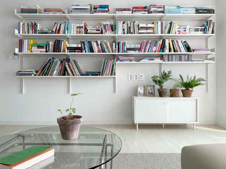 Natural living room in white and wood tones, featuring full wall bookshelf and white cabinet adorned with air-purifying plants