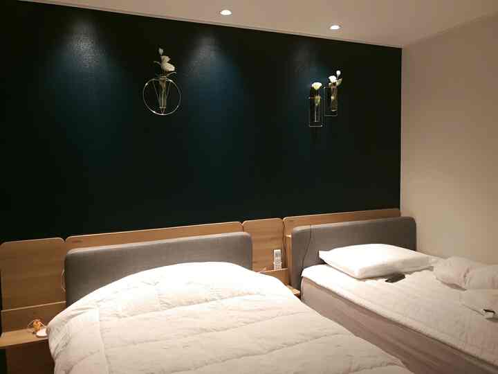 Hotel-like twin bedroom with deep green accent wall, gold vase decorations, and white bedding creating a cozy atmosphere