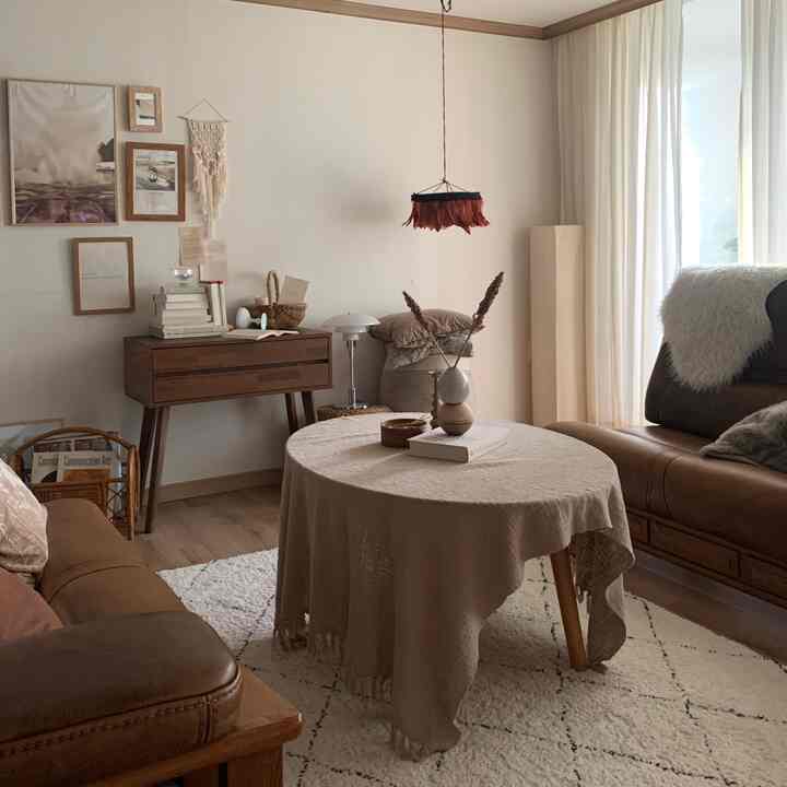 Natural-toned living room featuring brown leather sofas, wooden vanity console, beige curtains, and decorative objets creating a cozy atmosphere