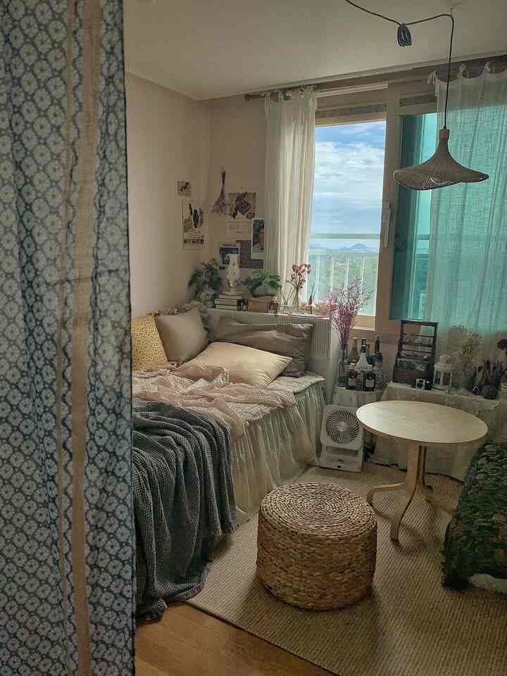 Natural-toned small bedroom featuring rattan stool, round table, and curtains with a cozy atmosphere