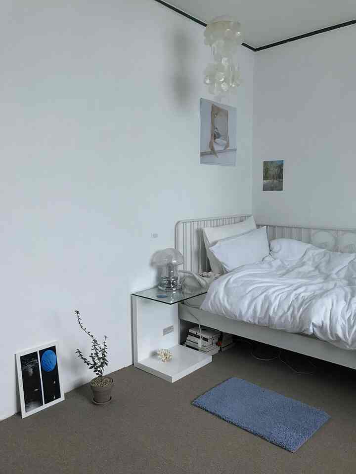 ホワイトとベージュのトーンの寝室、シンプルな家具とブルーのバスマットが配置された清潔感のあるインテリア