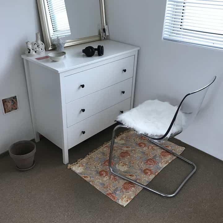 White-toned small closet and transparent chair on floral rug in a minimal and tidy room