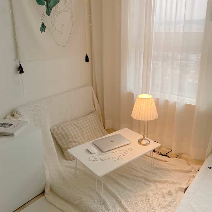 White and beige toned bedroom featuring a foldable table, sofa, and warm lighting creating a cozy workspace