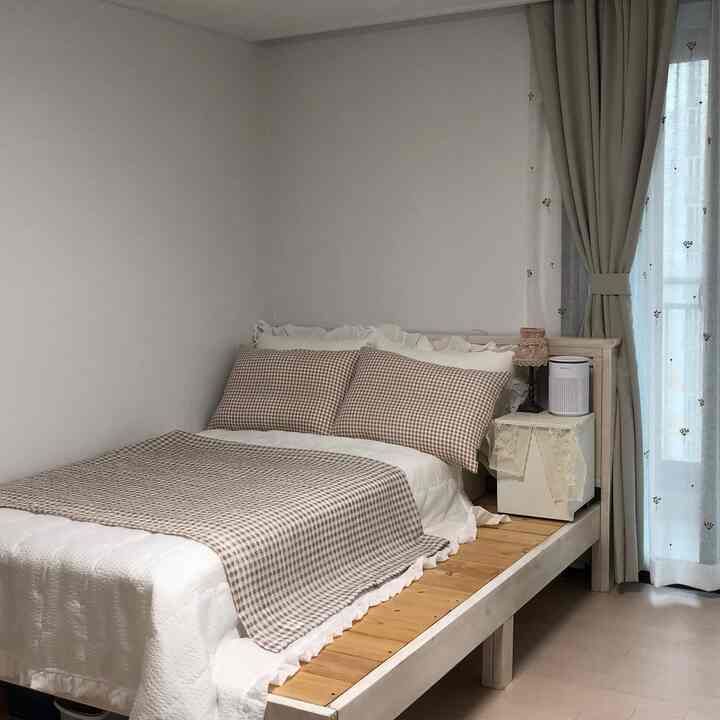 White and beige toned bedroom featuring a wooden bed, pillows, and curtains creating a cozy atmosphere
