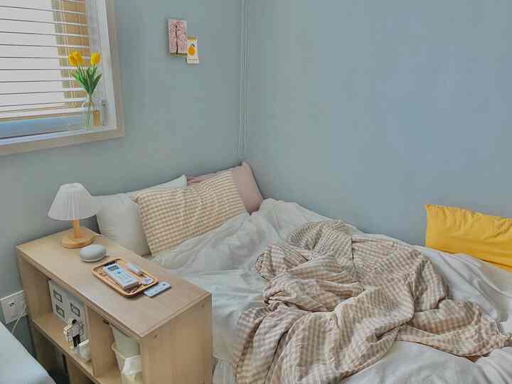 White and beige toned bedroom featuring checkered duvet cover, multiple pillows, and wooden storage shelf creating a cozy atmosphere