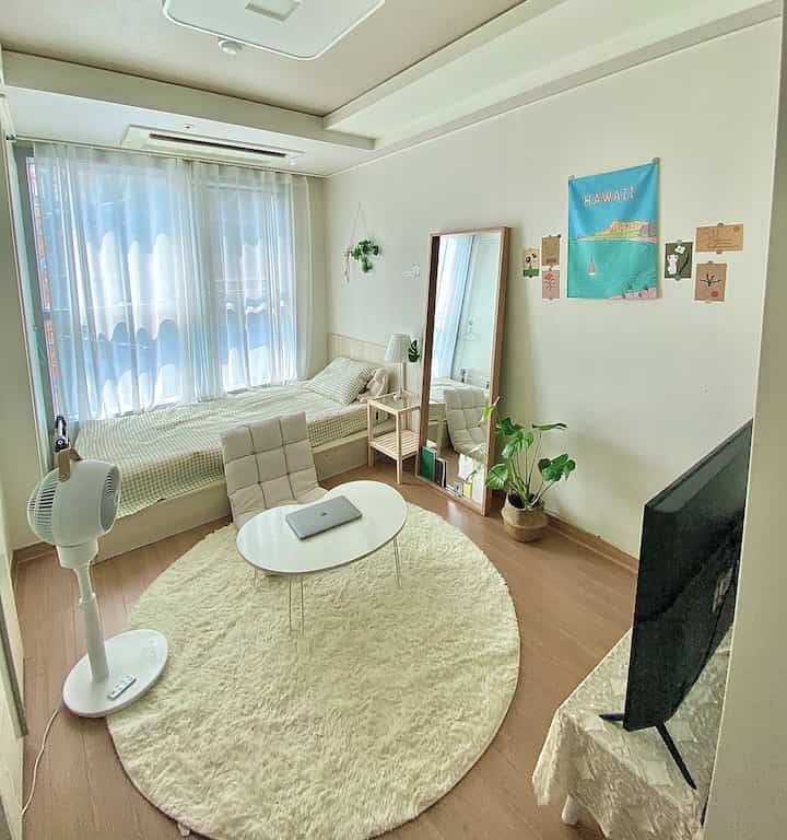 ホワイトとウッドトーンの調和が取れたコンパクトな寝室、ラウンドラグと座卓、シングルベッドと大型の鏡が配置された落ち着いた空間