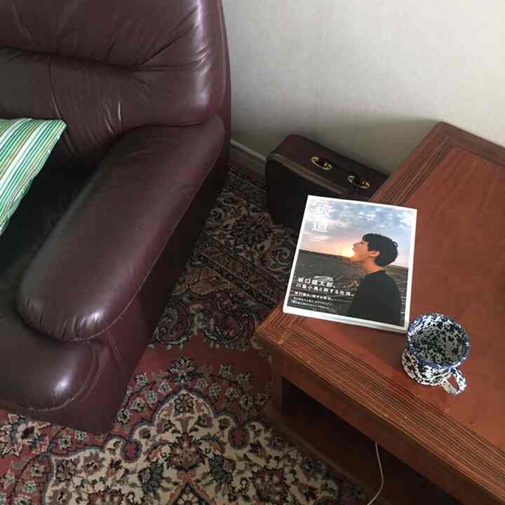 Natural-toned living room with a brown leather sofa and an oriental Persian rug, featuring a coffee table with a mug and book creating a cozy atmosphere
