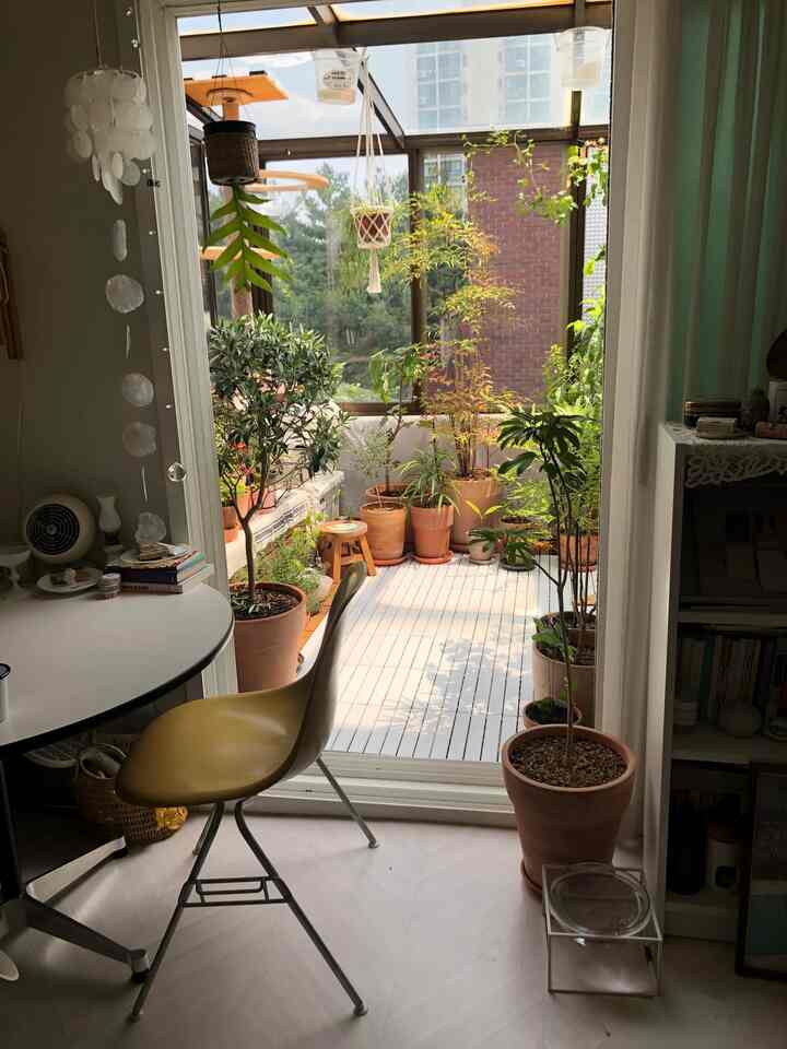 Bright white-floor natural veranda featuring various potted plants and an Eames chair in a cozy study setting
