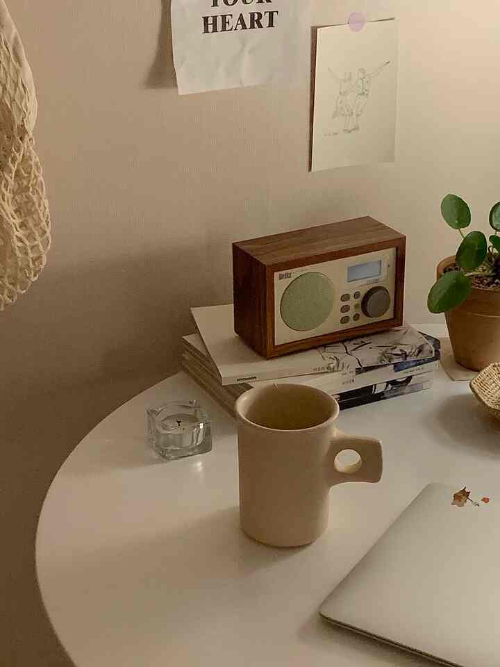 温かみのあるベージュとホワイトの色調の寝室の一角に、丸いテーブルの上にマグカップとブルートゥーススピーカー、観葉植物が置かれた雰囲気のあるインテリア