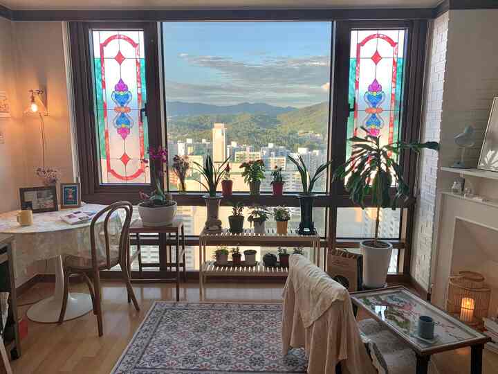 Living room with natural wood tones and vintage stained glass windows, featuring abundant plants and cozy lighting