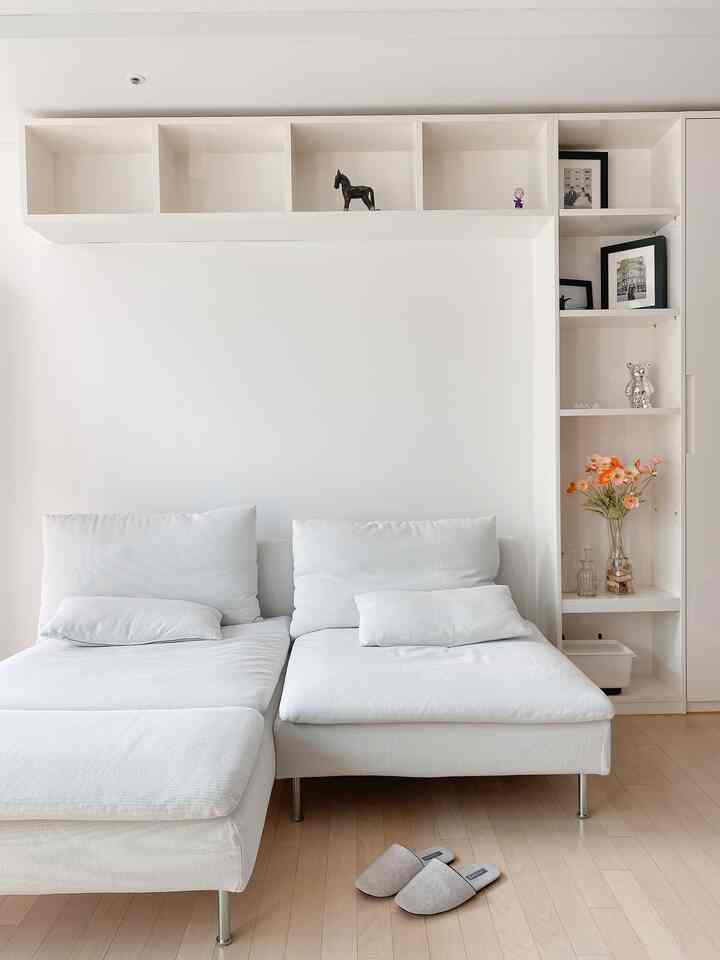 Bright white and wood-toned living room featuring a modern sectional sofa and clean shelving with decorative objets