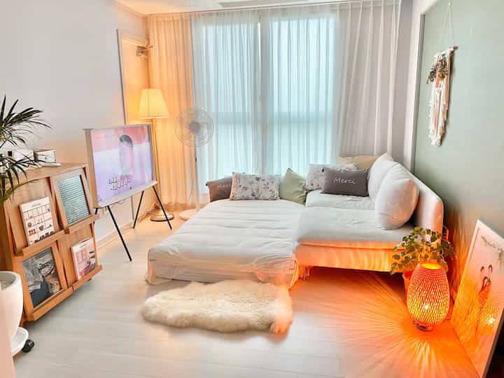 White and beige toned living room and bedroom featuring a sofa bed, rug, and orange mood lamp creating a cozy atmosphere
