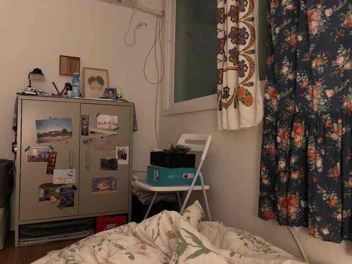 White and brown toned small bedroom featuring floral curtains and a cabinet, creating a cozy atmosphere