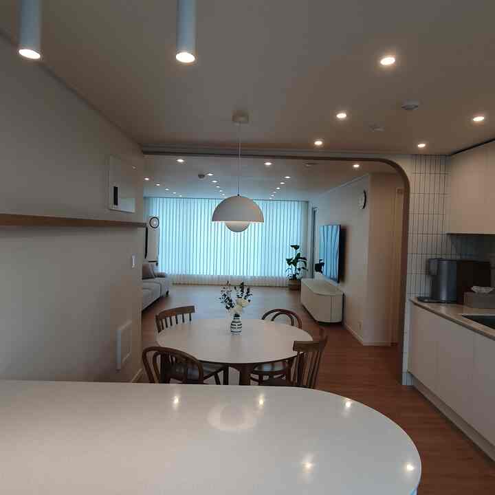White and wood tone kitchen and living room interior featuring rounded-edge island dining table and chairs, creating a simple and cozy space