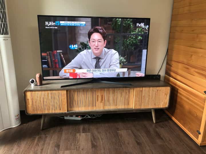 Brown wood tone flooring and wall blend in a living room featuring a retro wooden TV stand with a 65-inch TV centered