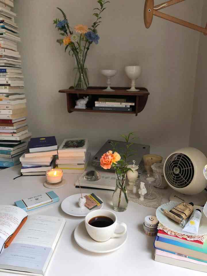 White-toned living room desk area featuring coffee cup, candle, flowers, and incense in a cozy Nordic style interior