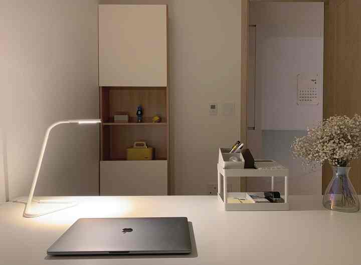 Minimal workspace with harmonious white and wood tones, featuring LED desk lamp, organizer on desk, and bookshelf in background