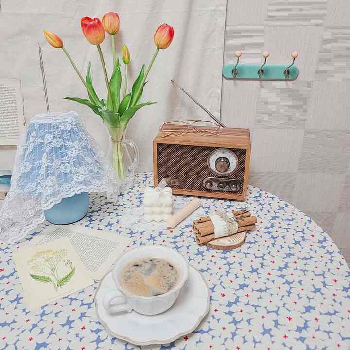 Cozy home cafe space featuring a coffee cup on a patterned tablecloth, vintage radio, artificial tulips, and candles