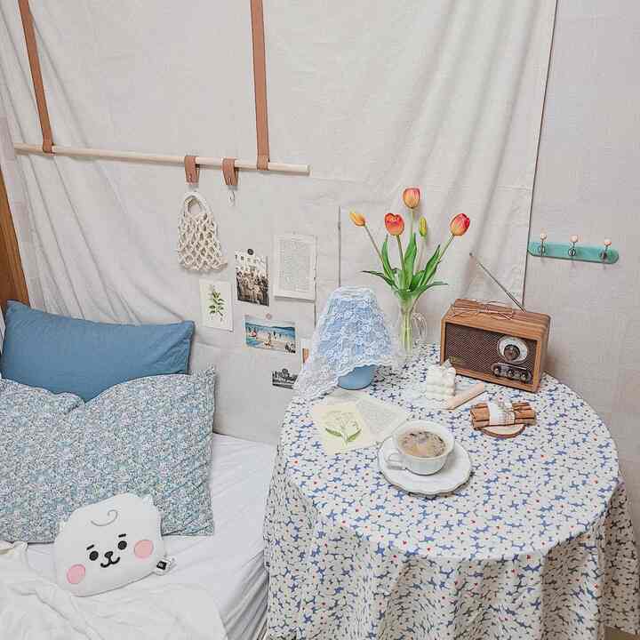 White and blue toned studio bedroom featuring a small table with a vase of tulips and a coffee cup creating a cozy summer interior