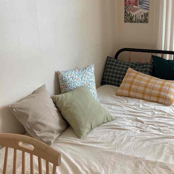 Beige natural-toned bedroom featuring a bed with multiple patterned cushions, presenting a cozy and fresh summer vibe