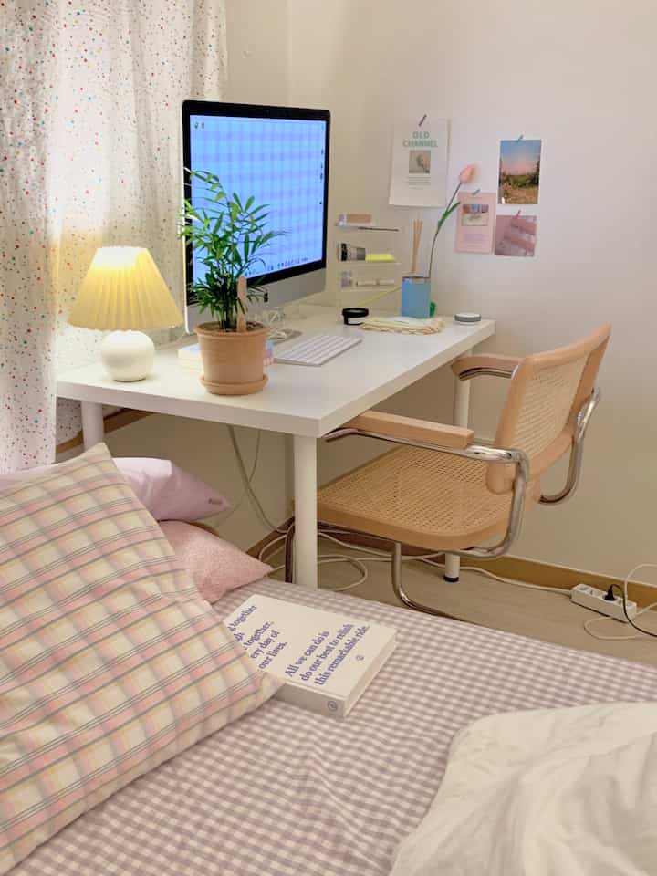 White and natural toned single household bedroom home office featuring a clean desk, lamp, and plant for a cozy atmosphere