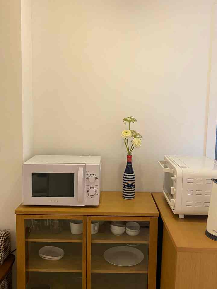 A simple kitchen with white and brown wood tones, featuring a microwave and oven on wooden cabinets