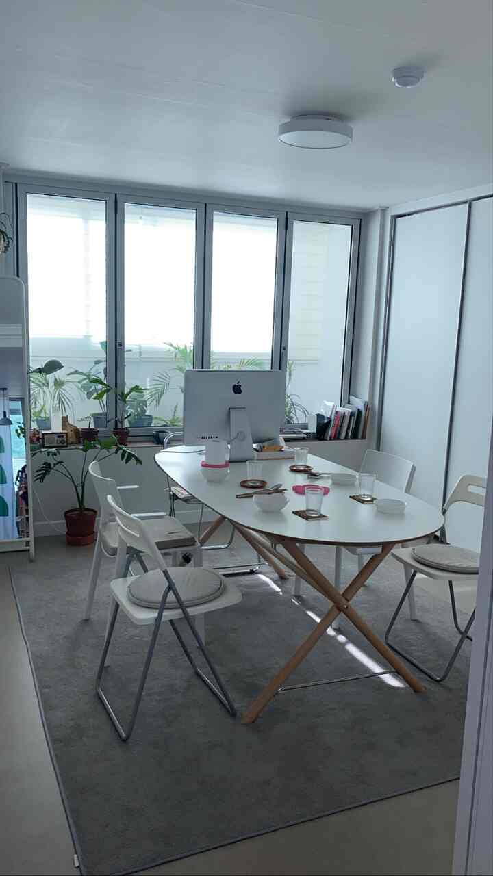 白と木目調が調和したダイニングルームで、中央にテーブルと椅子が配置され、コンピュータが置かれたモダンなホームオフィス空間です。