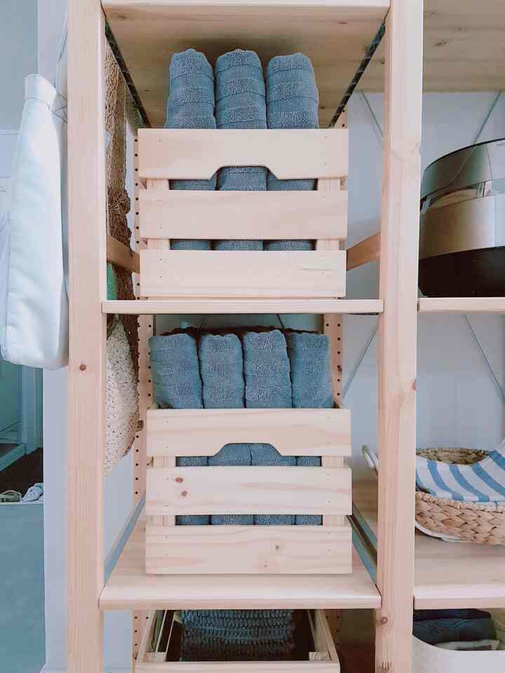 ナチュラルな木目調のバスルームの棚に青いタオルが整然と収納された清潔感のある空間