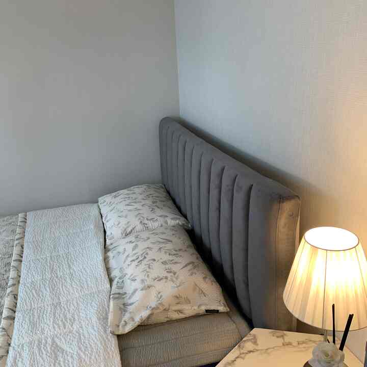 Cozy bedroom with gray velvet headboard, white walls, marble side table, and a glowing table lamp