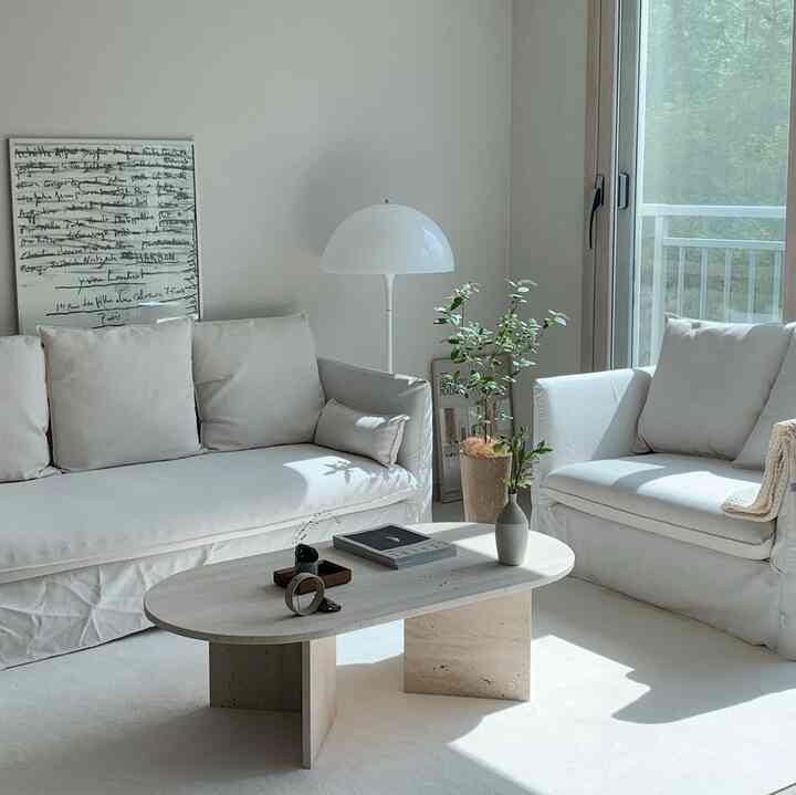 Natural color living room featuring white sofas, stone coffee table, floor lamp, and green plant with a comfortable warm atmosphere