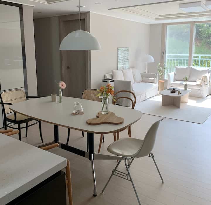Bright white-toned kitchen and living area featuring an island dining table with diverse dining chairs in a natural modern style interior