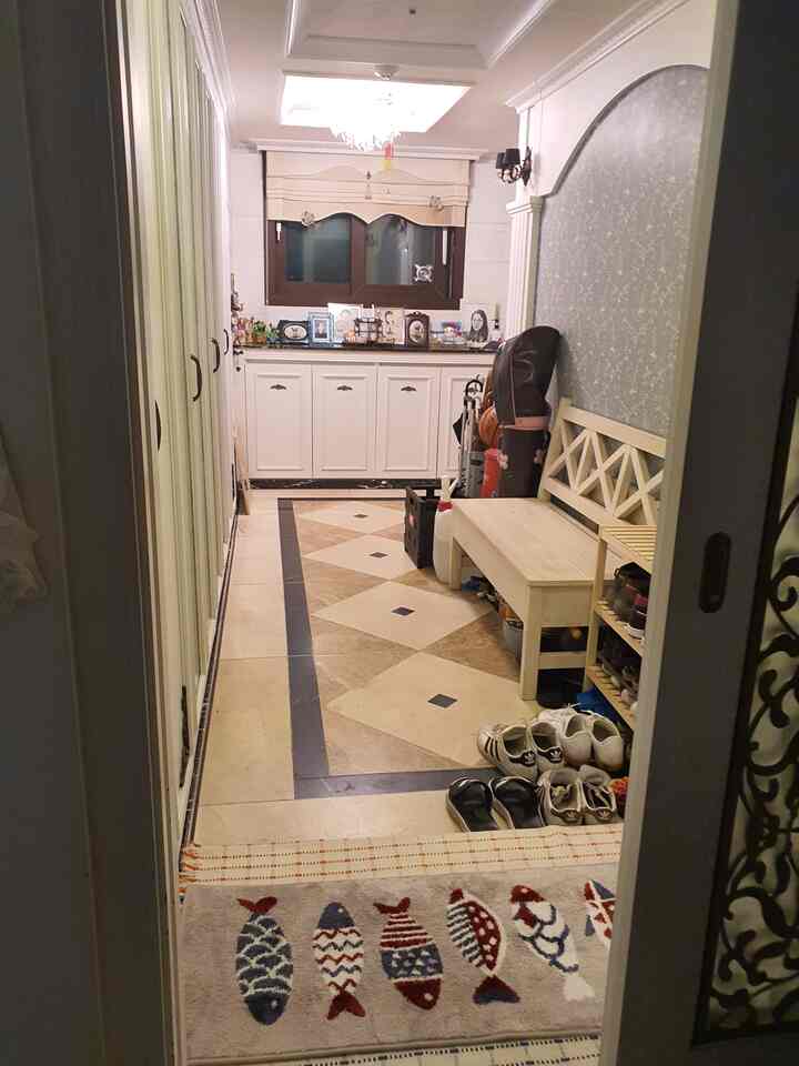 ホワイトと木目調の配色の廊下型玄関、シューズキャビネットとベンチが配置された雰囲気のある空間