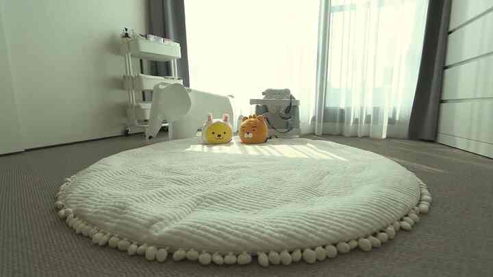 A white and gray toned kids' room featuring a large white round rug with plush toys arranged center, creating a cozy and clean atmosphere