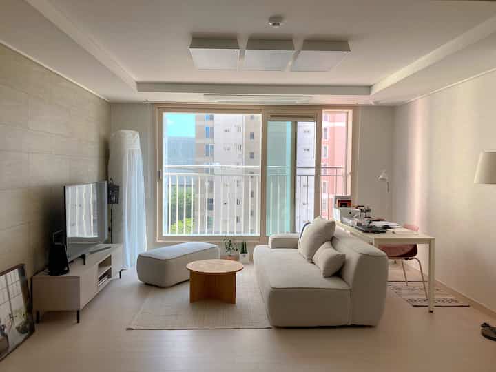 白とナチュラルカラーのリビング、ソファと丸テーブル、デスクが配置された雰囲気のあるインテリア