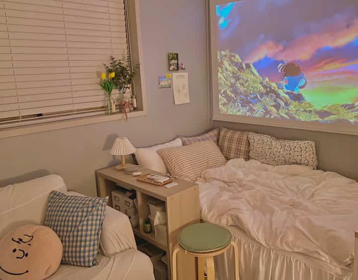Beige and white toned studio apartment living room featuring sofa and bed with cozy home cinema atmosphere