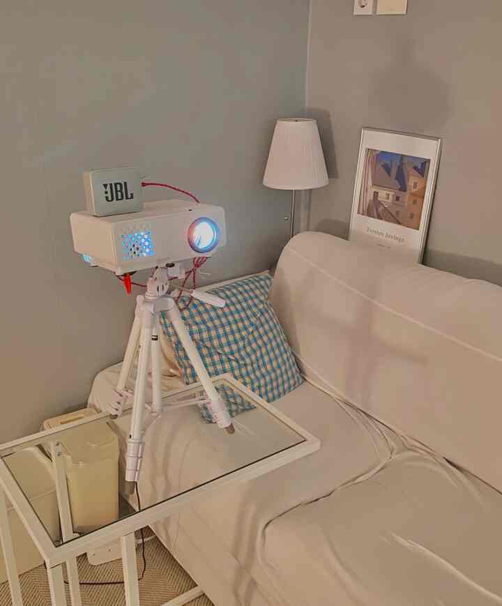 White and gray toned living room featuring a projector, sofa, side table, table lamp, and poster with cozy home cinema atmosphere