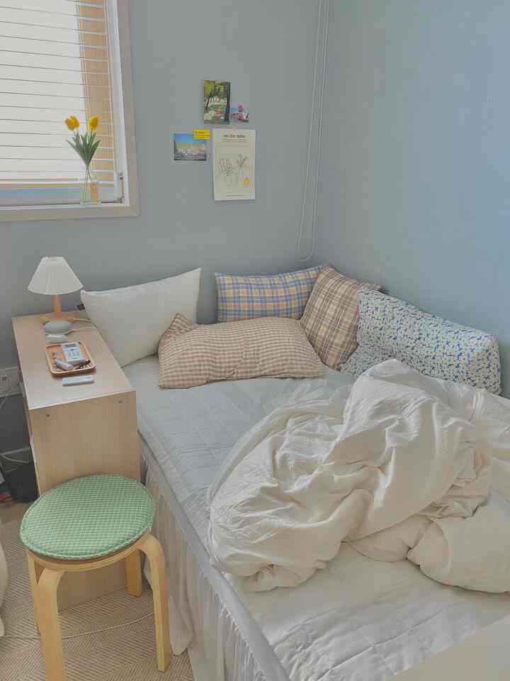 Soft blue walls and white bedding blend in a cozy bedroom, featuring pillows and a stool for comfort