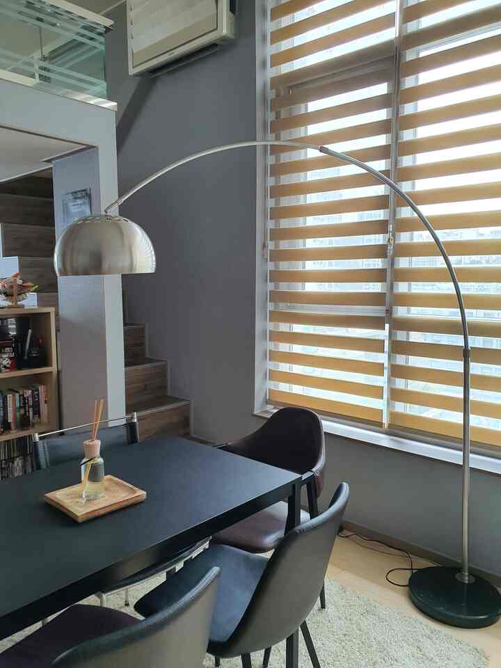 Gray-toned dining room with silver steel floor lamp and blinds, featuring a black dining table with four chairs in a modern setting