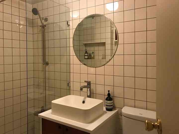 White tiled wall bathroom featuring a round mirror, sink, and toilet with a clean and minimal atmosphere