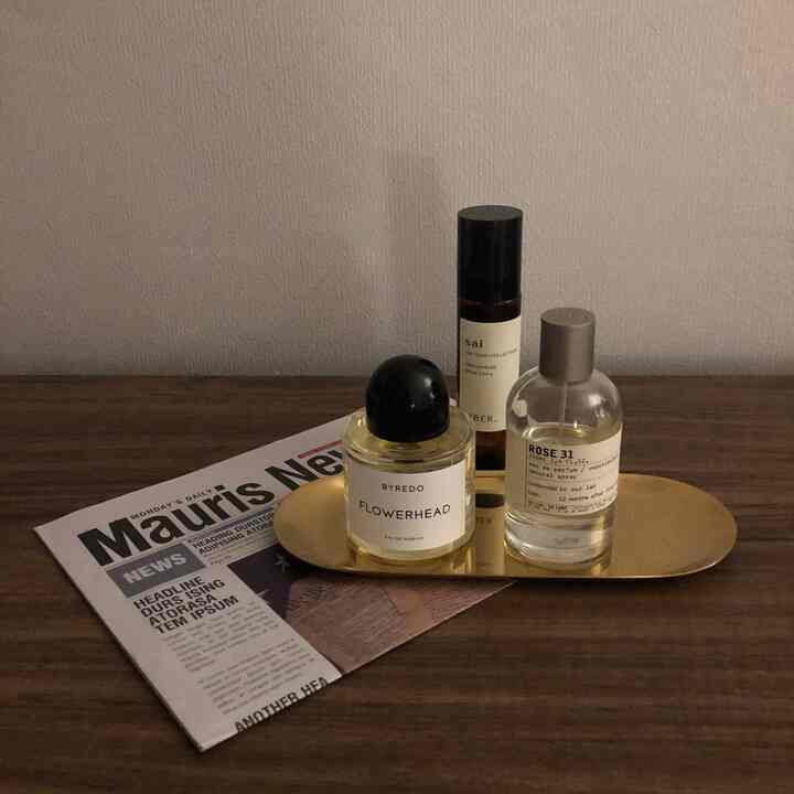 茶色の木製収納棚の上にゴールドのトレイと香水瓶、英字新聞が置かれたシンプルなインテリア小物の配置