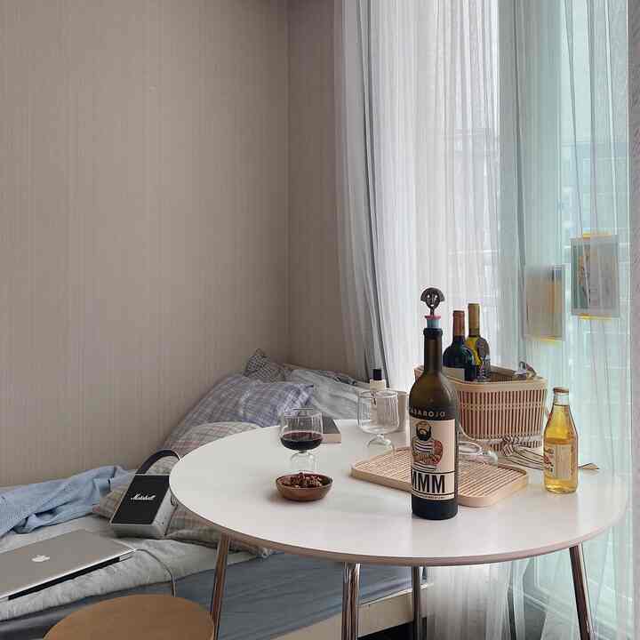 Natural color small room featuring a round white table and stool, with wine bottles and glasses creating a cozy home bar atmosphere